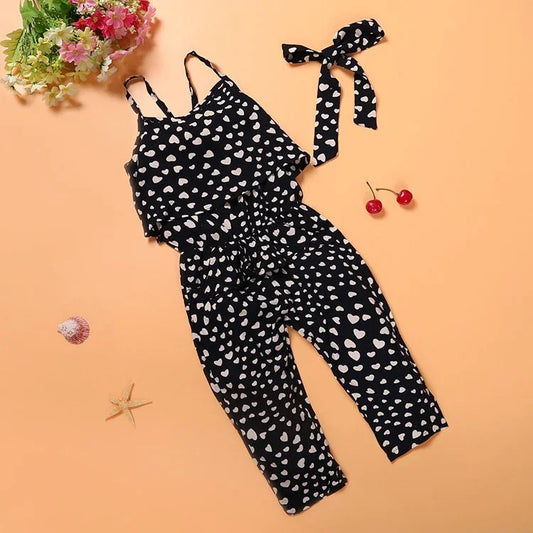 Girls black heart print jumpsuit with matching headband on peach background