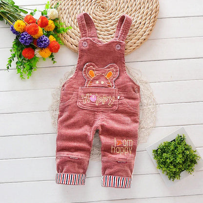 Pink corduroy baby overalls with bear face and 'Happy' text, styled with floral decor.