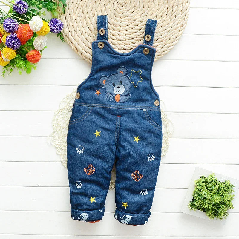 Blue denim baby overalls with bear and star embroidery, flat lay on white wooden background