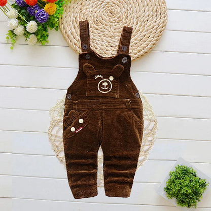 Brown corduroy baby overalls with bear face embroidery on white wooden background