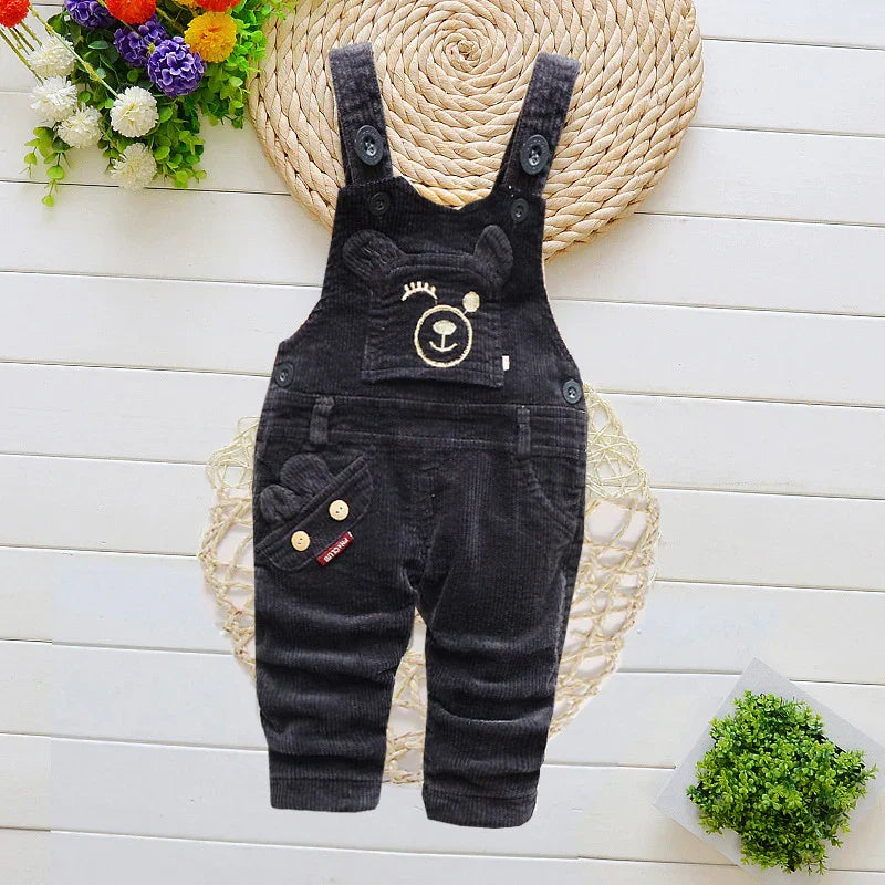 Black corduroy baby overalls with bear face embroidery, flowers and plants background
