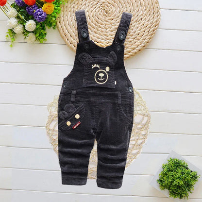 Black corduroy baby overalls with bear face embroidery, flowers and plants background
