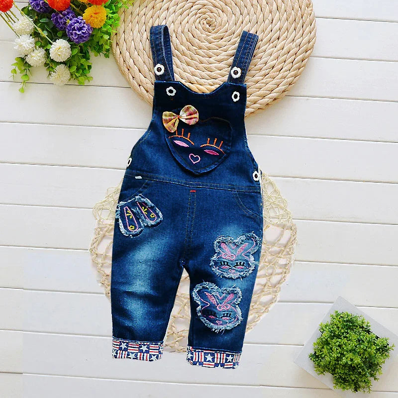 Kids denim overalls with colorful face and animal patches, floral decor, flat lay