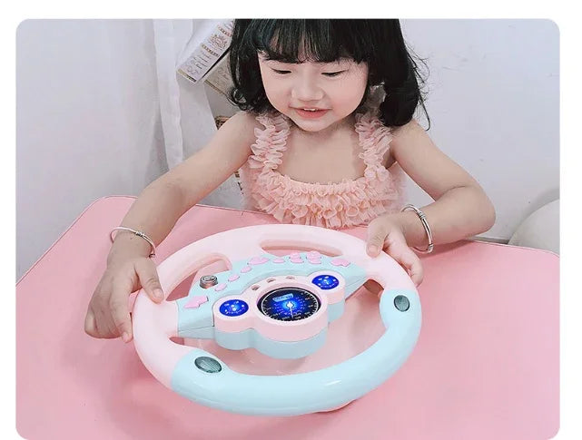 Smiling girl playing with pink and blue toy steering wheel at a table