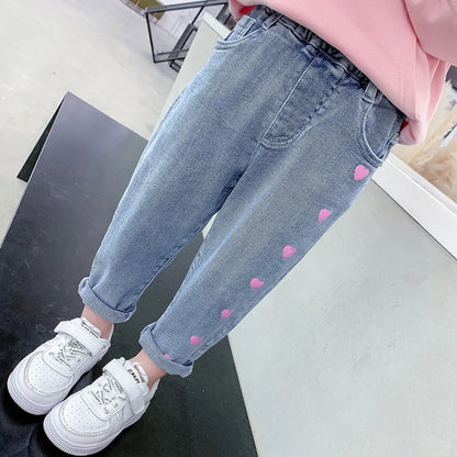 Girl wearing light blue jeans with pink hearts and white sneakers indoors