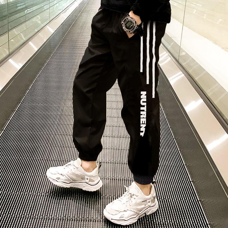 Black jogger pants with white stripes and NUTRENT logo, worn with white sneakers in a modern hallway
