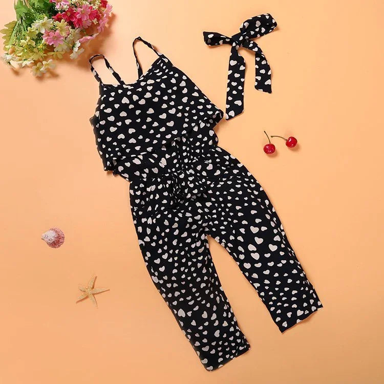 Girls black heart print jumpsuit with matching headband on peach background
