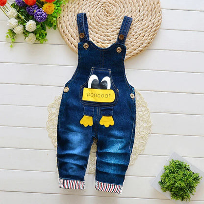 Denim baby overalls with cartoon eyes and 'pancoat' text, on a white wooden background