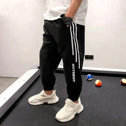 Man in black joggers with white stripes and 'NUTRENT' text, white sneakers, standing by a pool table