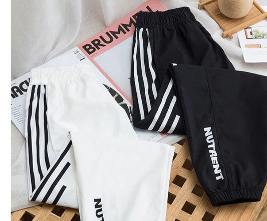 Black and white jogger pants with stripes and NUTRENT logo on wooden surface
