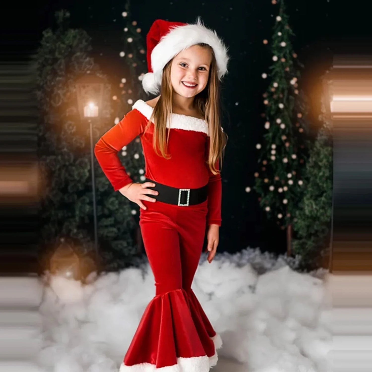 Smiling girl in a red Santa suit and hat, Christmas trees and lights in snowy background