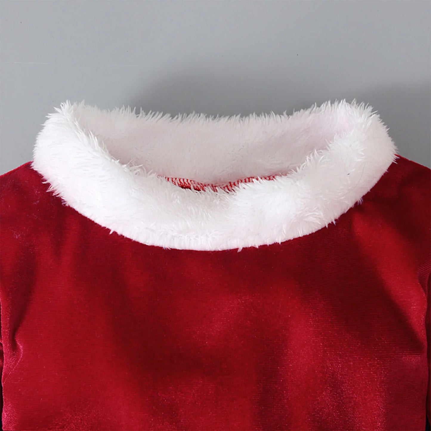 Red velvet top with white faux fur collar on gray background, festive clothing detail