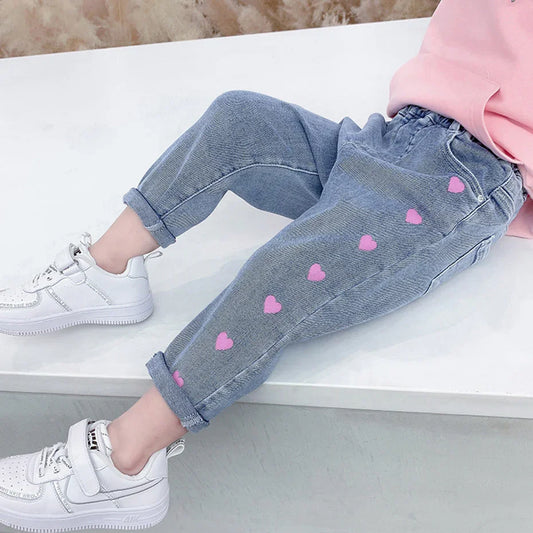 Child in light blue jeans with pink heart prints, white sneakers, and pink sweatshirt