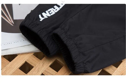 Black jogger pants with elastic cuffs on a wooden surface, partial white text visible