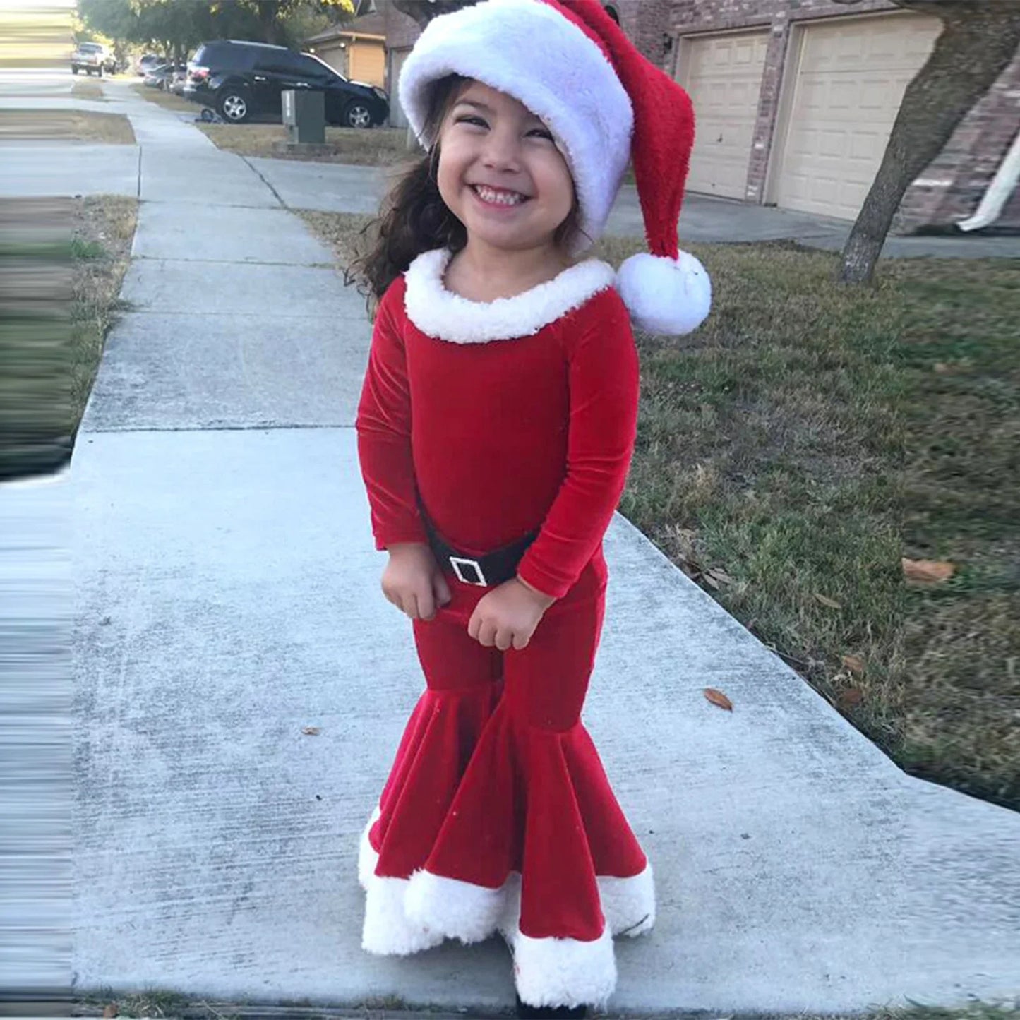 Smiling young girl in red Santa dress and hat standing on sidewalk outdoors